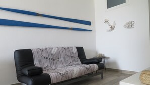 A modern living room with a black leather sofa, a small side table, and a wall-mounted shelf with blue objects. - SeaHouse (Torre Vado marina di morciano di leuca)