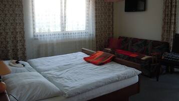 Une chambre d’hôtel avec un lit, un canapé, une télévision et une fenêtre avec des rideaux.