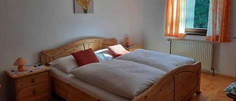 Een houten bed met twee kussens, een nachtkastje met een lamp en een raam met gordijnen.