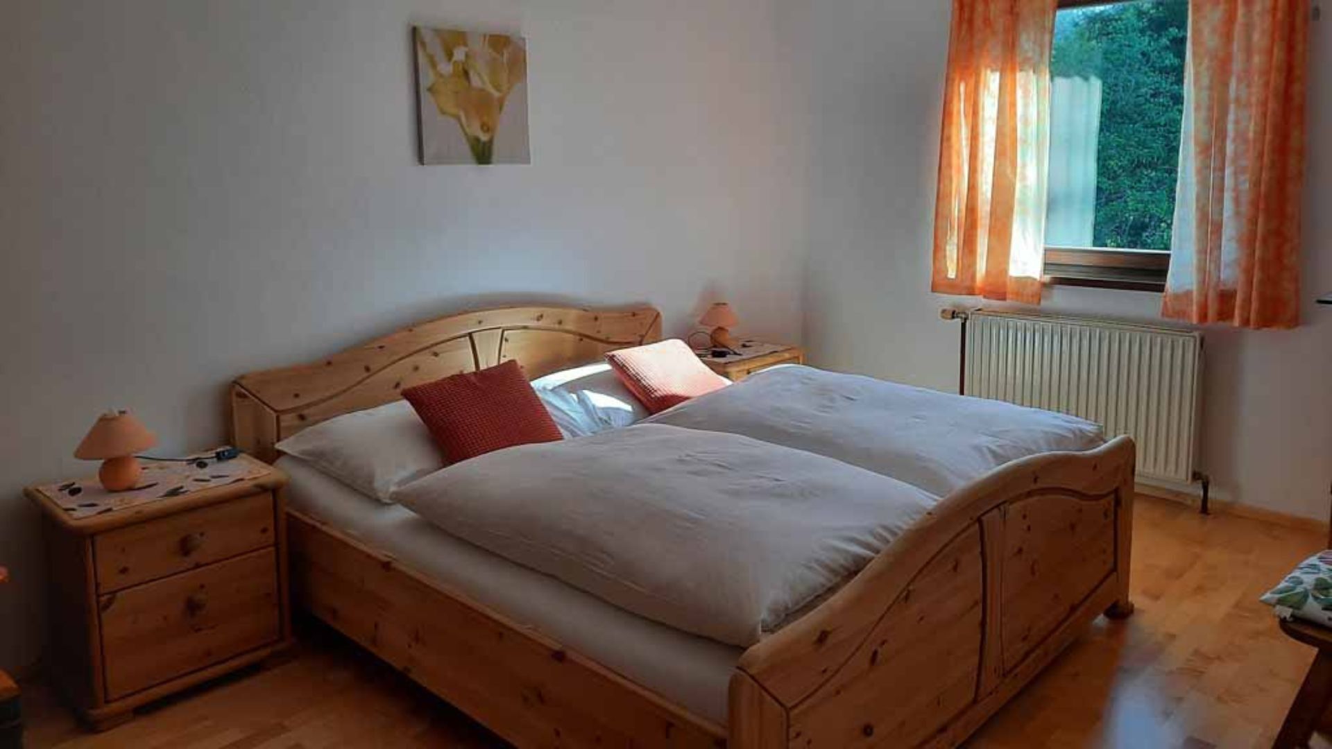 Un lit en bois avec deux oreillers, une table de chevet avec une lampe et une fenêtre avec des rideaux.