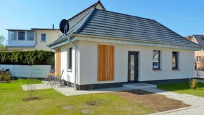 Une maison moderne de plain-pied, dotée d’un toit en pente, d’un petit porche à l’avant et d’une pelouse bien entretenue.
