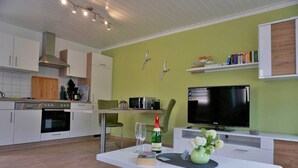Une cuisine moderne avec des armoires blanches, un four encastré et un coin repas avec une table dressée pour deux personnes.