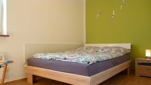 Une chambre à coucher avec un lit, une table de chevet, une lampe et un mur décoré avec un motif d’oiseau.