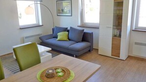 Un salon moderne avec un canapé gris, une table à manger agrémentée d’un set de table vert et un meuble blanc aux portes en verre.
