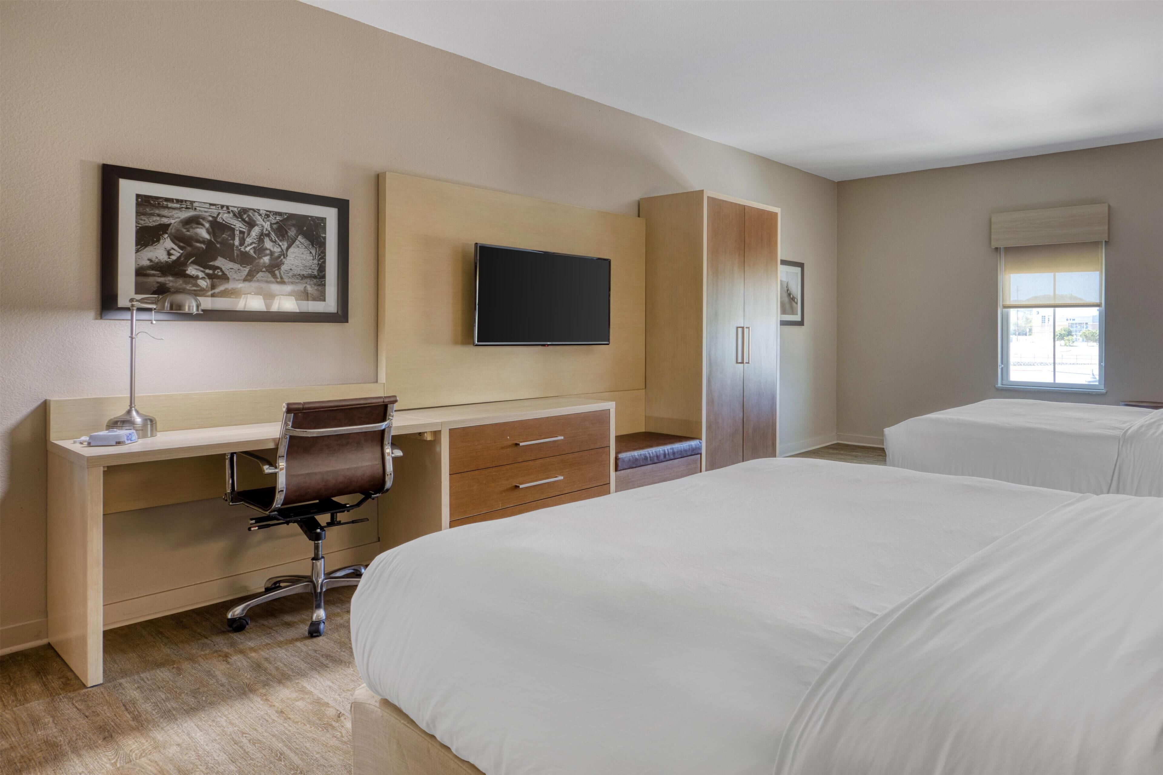 A hotel room with a bed, a desk with a chair, a television, and a wardrobe.