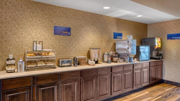 Een ontbijtbuffet met diverse etenswaren en drankjes, waaronder een koffieapparaat en een koelkast.