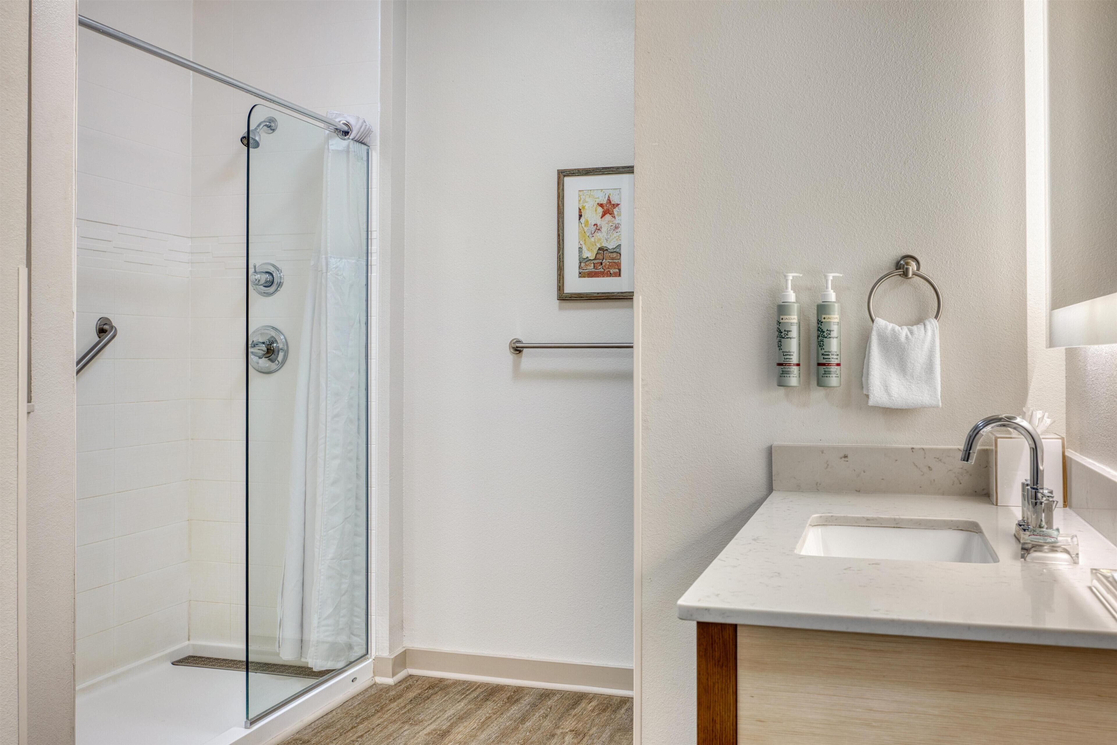 A bathroom with a glass shower enclosure, a sink with a marble countertop, and toiletries on the wall.