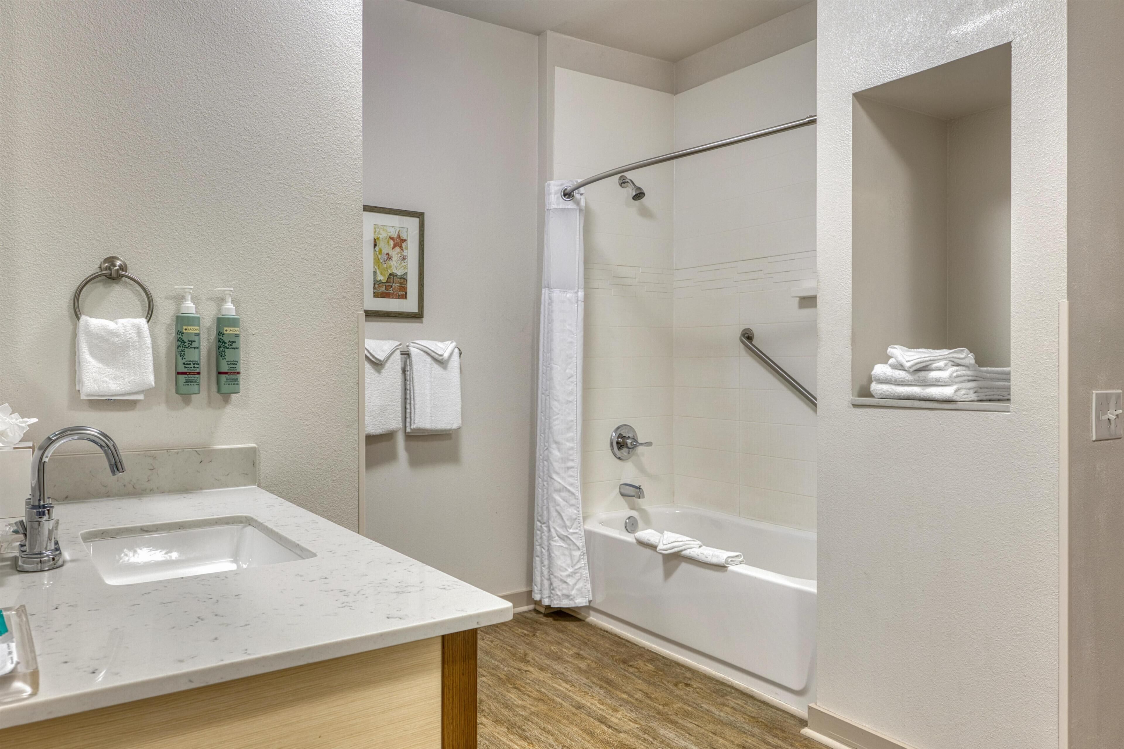 A bathroom with a sink, shower, and a shelf with towels.