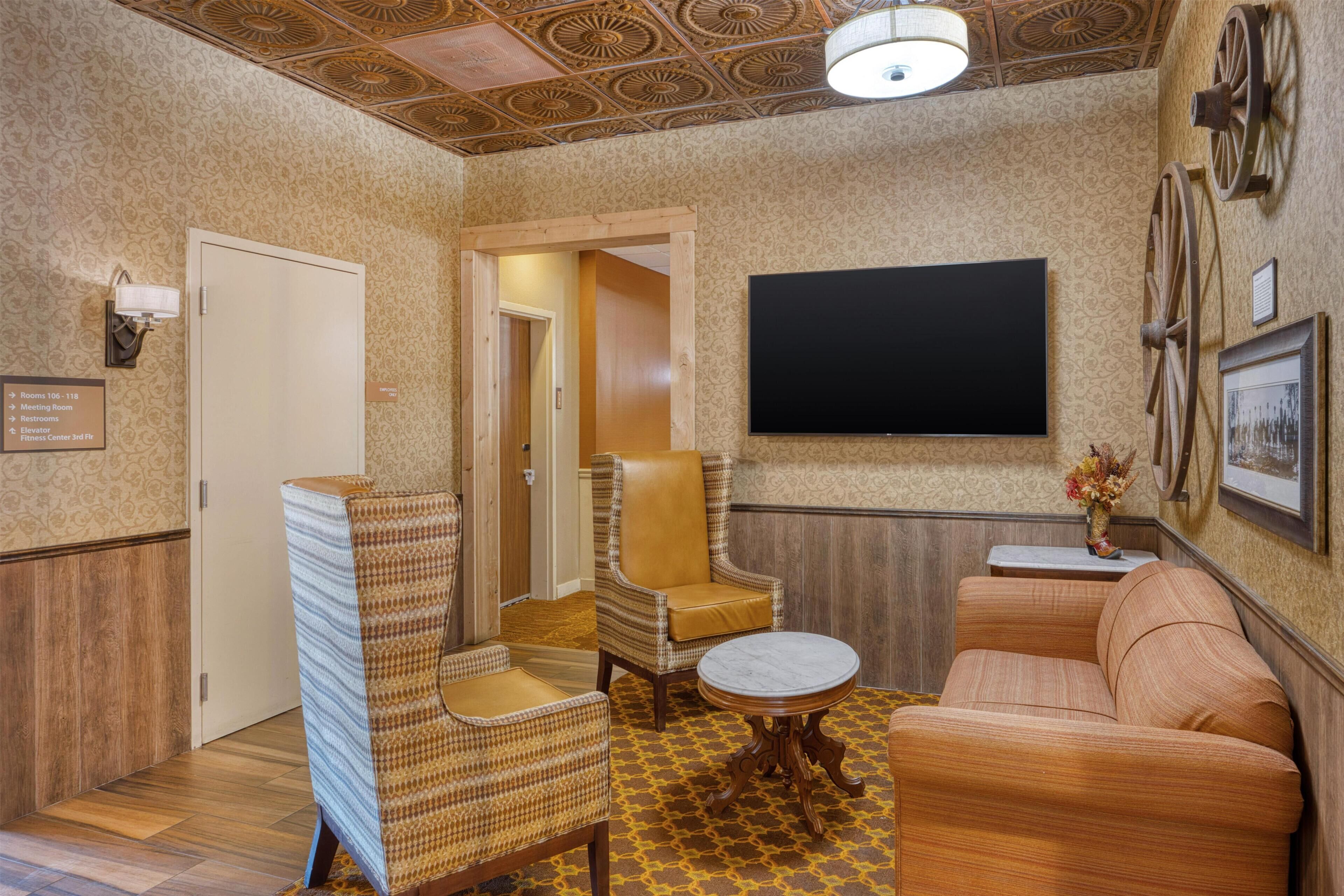 A room with a patterned wall, a flat-screen TV, wicker furniture, and a wooden floor.