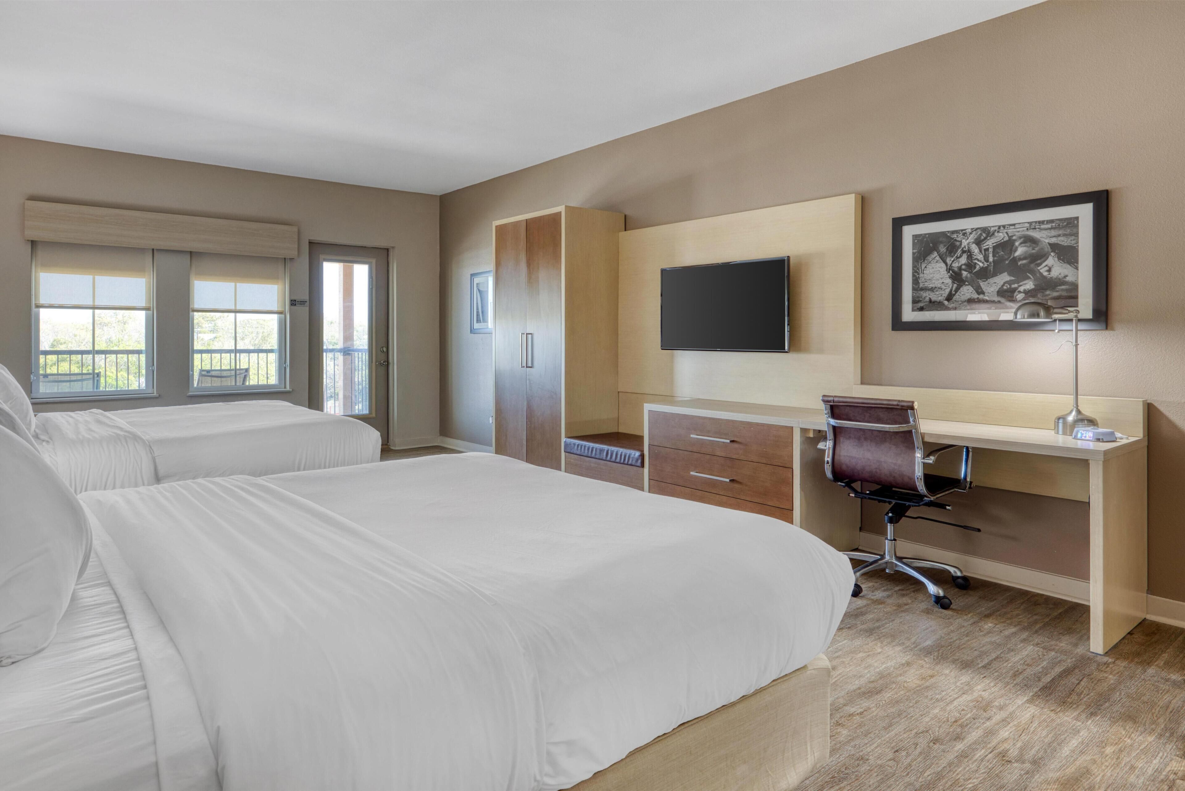 A hotel room with two beds, a desk, a chair, a flat-screen TV, and a framed picture on the wall.