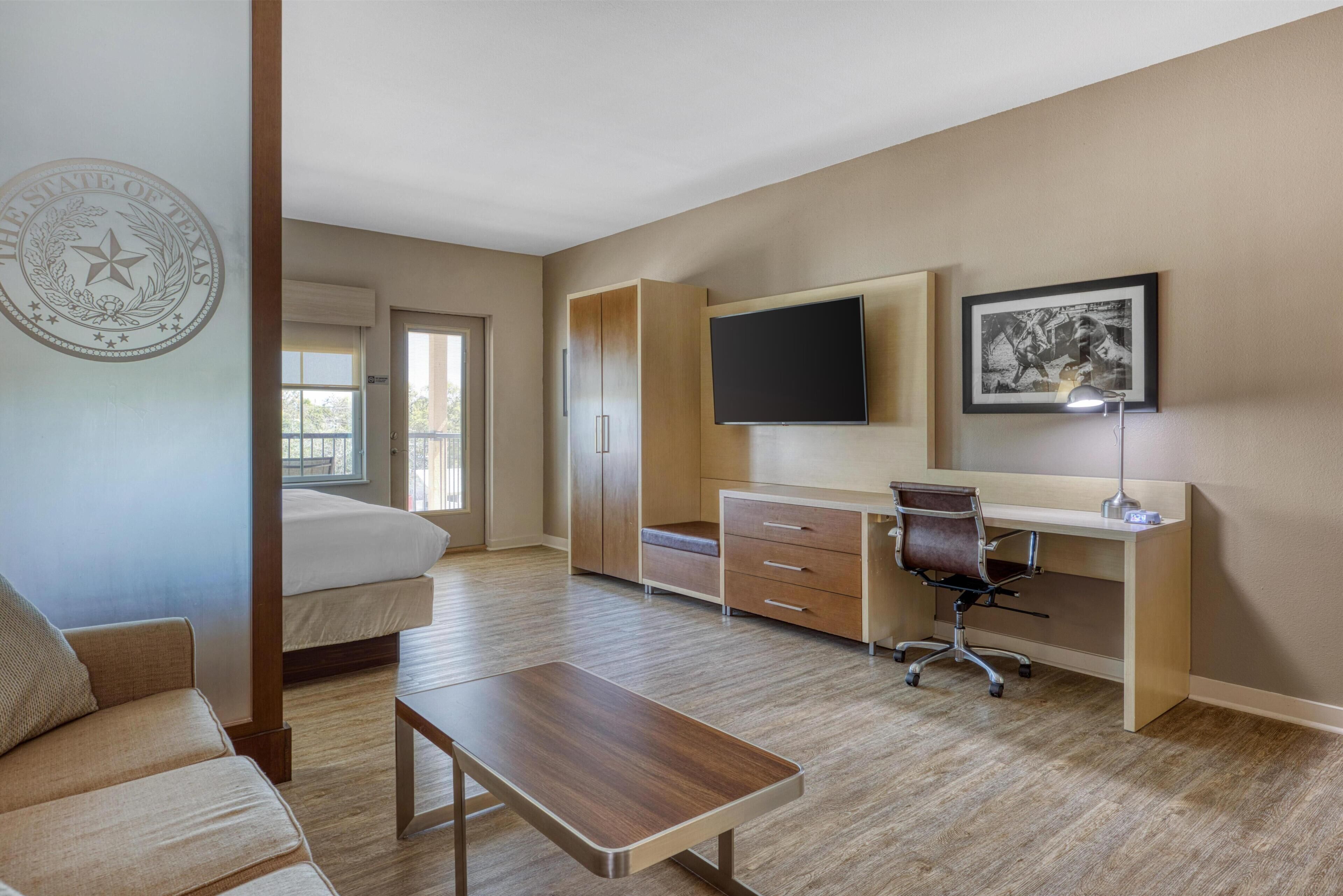 Une chambre d’hôtel avec un lit, un bureau et une chaise, une télévision, un tableau encadré et une fenêtre.