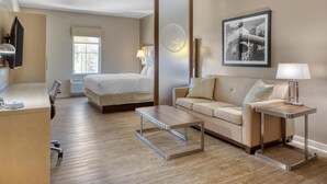 A hotel room with a bed, a sofa, a desk, a chair, a mirror, and a framed picture on the wall. - Best Western Bandera Suites & Saloon (Bandera)