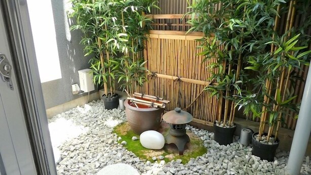 A small outdoor garden area with a bamboo fence, potted plants, a stone lantern, and a traditional Japanese tea urn. - Pacio Nijo (Kyoto)