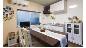 A compact kitchen with a dining area, white cabinetry, a built-in oven, and a window. - Pacio Nijo (Kyoto)