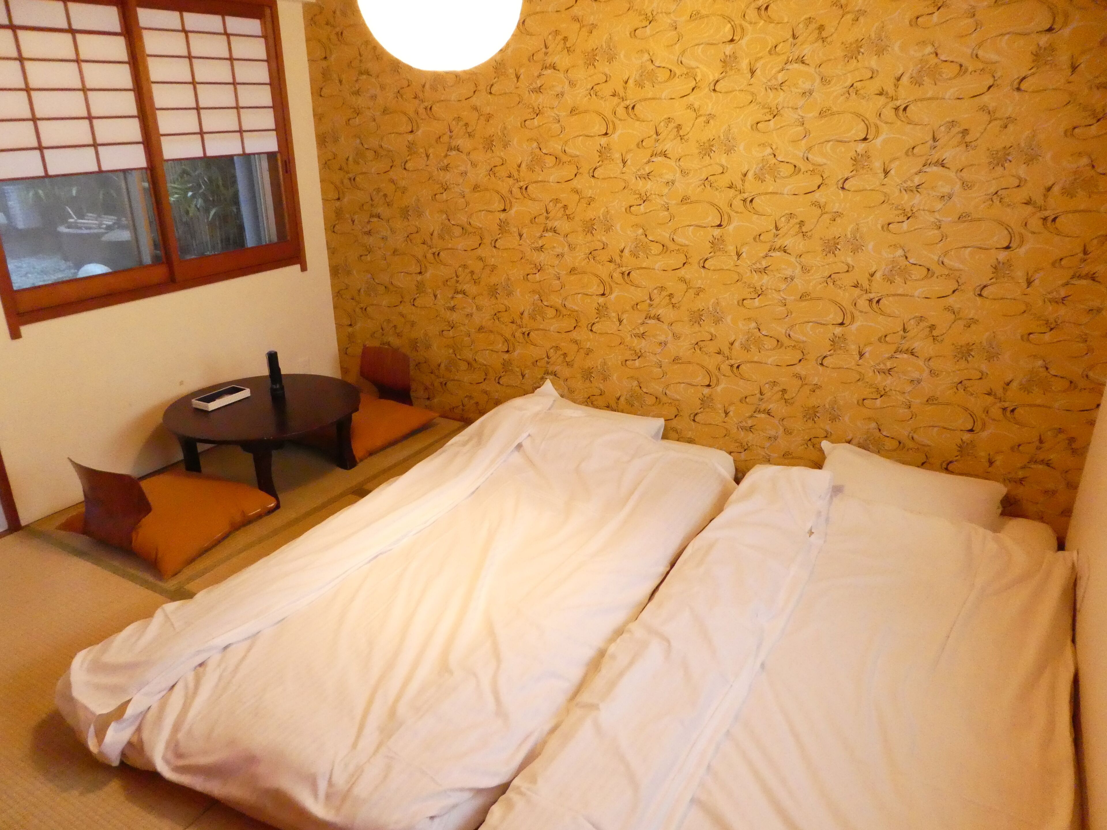 Una habitación de hotel con una cama, una mesita con una silla y una ventana que ofrece vistas al verde exterior.