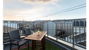 A balcony with a table and chairs, overlooking a body of water and industrial structures. - Pacio Nijo (Kyoto)