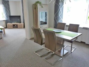 Ein moderner Essbereich mit Tisch, Stühlen und einem Fernseher im Hintergrund.