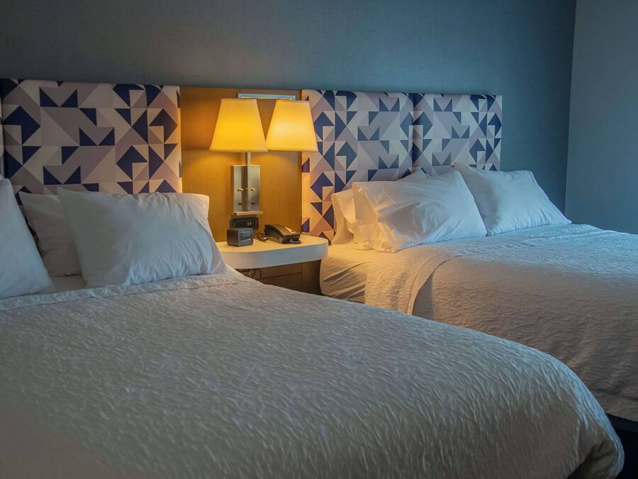 Ein Hotelzimmer mit zwei Betten, einem Nachttisch mit Lampe und einem Kopfteil mit geometrischem Muster.