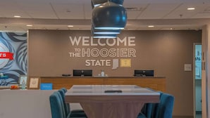 A reception area with a 'Welcome to the Hoosier State' sign, a reception desk, and a seating area with a table and chairs. - Hampton Inn Wabash (Wabash)