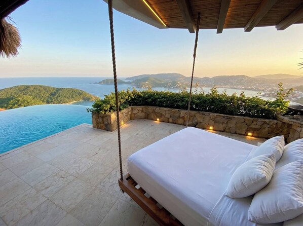 Une chambre avec un lit suspendu, une vue sur la mer et un mur de pierre orné de plantes.