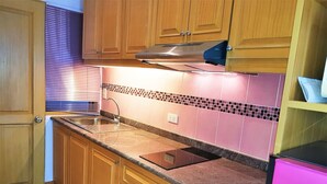 Une cuisine avec des meubles en bois, une hotte de cuisinière en acier inoxydable, un évier et un dosseret de carrelage rose.