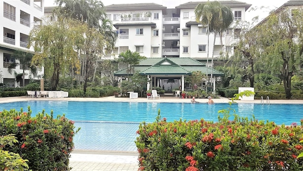 Une piscine entourée d’une végétation luxuriante et un immeuble à plusieurs étages doté de balcons.