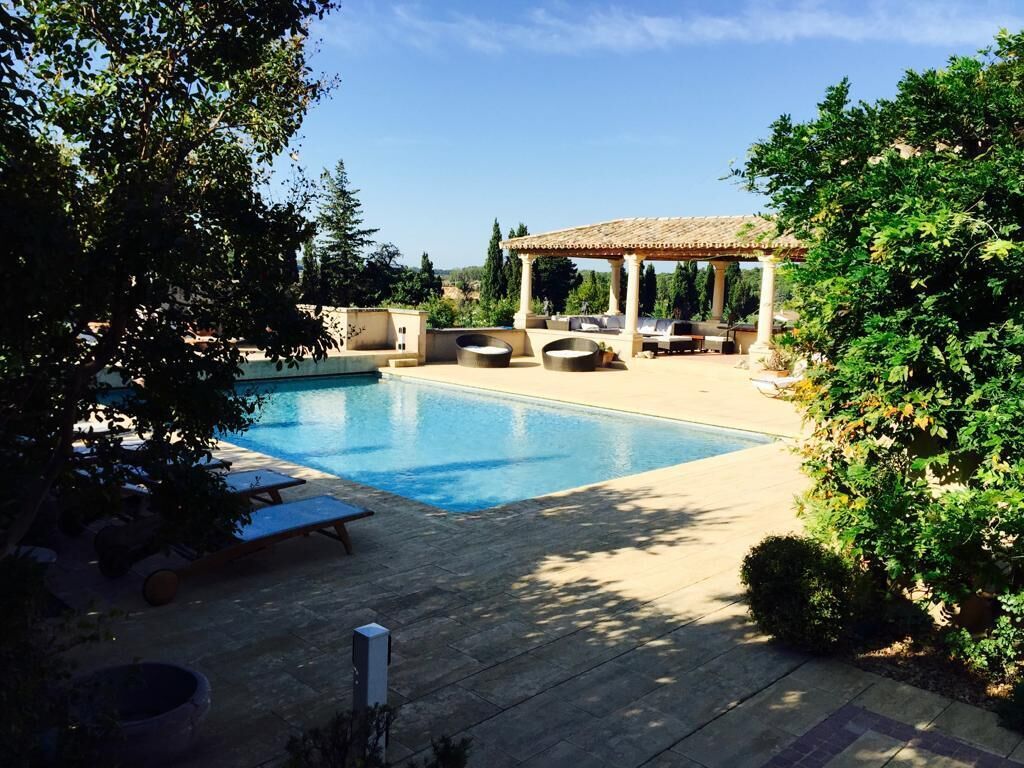 A swimming pool with a pergola and lounge chairs, surrounded by greenery.