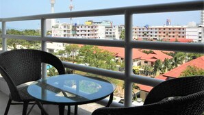 A balcony with wicker chairs and a glass table, overlooking a cityscape with buildings and a tower. - View Talay 2A, 5th Floor Studio Condo (Pattaya)