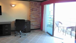A room with a desk, chair, and a sliding glass door leading to an outdoor area with chairs. - View Talay 2A, 5th Floor Studio Condo (Pattaya)