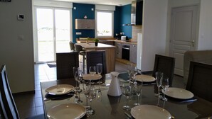 Een moderne eetruimte met een tafel gedekt voor zes personen, een keuken op de achtergrond en uitzicht door de glazen deur.