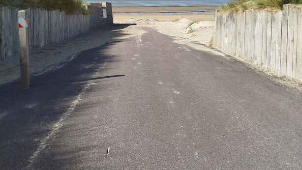 Een verhard pad dat naar een strand leidt, met houten omheiningen aan beide kanten.