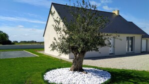 Een huis met een witte gevel, een grijs dak en een boom in de voortuin.