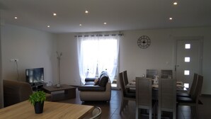 Een moderne woonkamer met een televisie, bank, eettafel, stoelen en een plant.