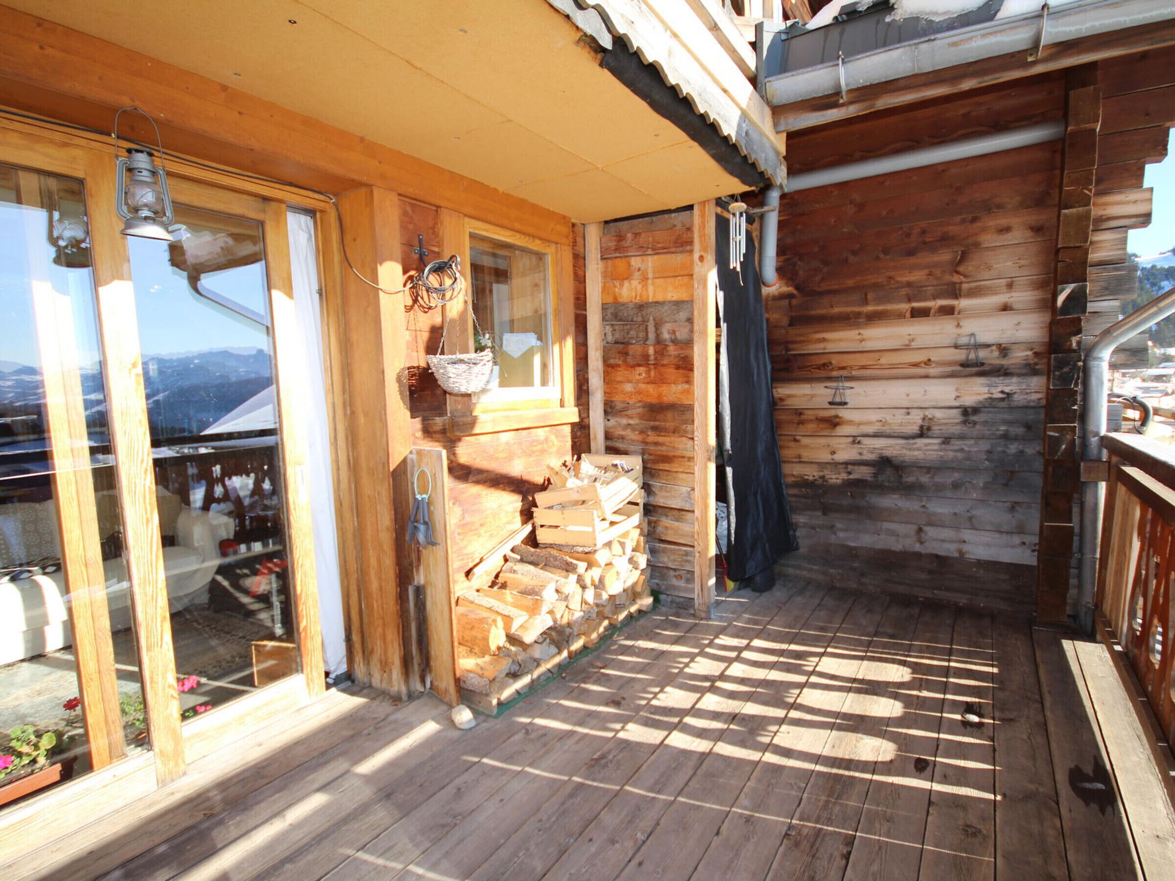 Une cabane en bois dotée d’un balcon, de grandes fenêtres et d’une pile de bois de chauffage.