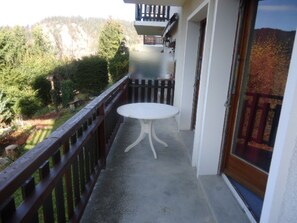 A balcony with a table and a wooden railing, overlooking a garden and forested area.