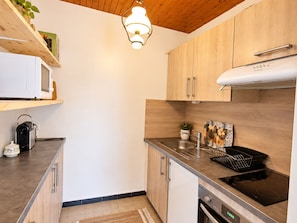 A modern kitchen with wooden cabinets, a stainless steel sink, and an induction cooktop. - 4-person ski-in apartment with parking (La Clusaz)