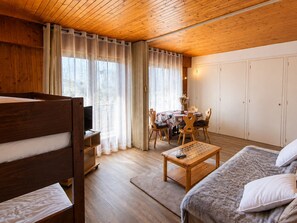 A cozy room with a wooden ceiling, a bed with white bedding, a small table with a remote control, a dining table with chairs, and a wardrobe. - 4-person ski-in apartment with parking (La Clusaz)