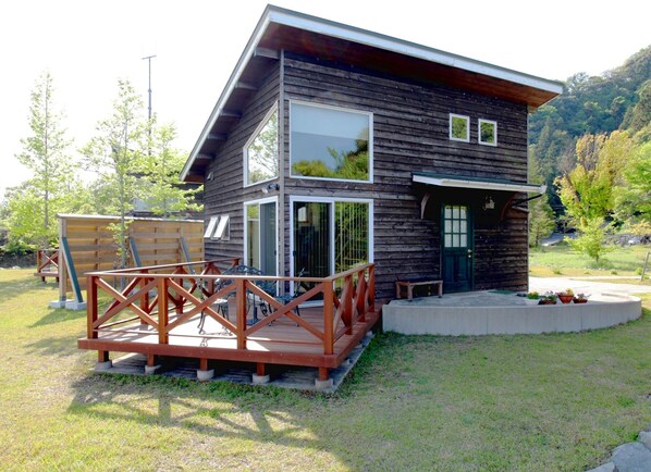 A modern two-story wooden house with a deck, large windows, and a green door.