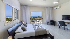 Ein modernes Hotelzimmer mit einem großen Bett, einem Fernseher, einem Schreibtisch und einem Balkon mit Blick.