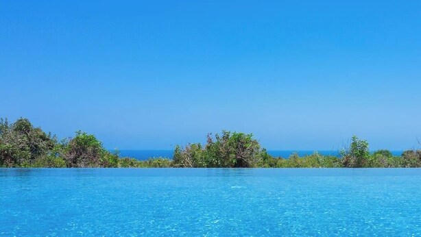 Ein klares, blaues Schwimmbecken mit Blick auf das Meer und üppiger Vegetation im Hintergrund.