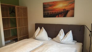 Una cama doble con ropa de cama a rayas y dos almohadas, un armario de madera y un cuadro de un atardecer sobre un muelle.