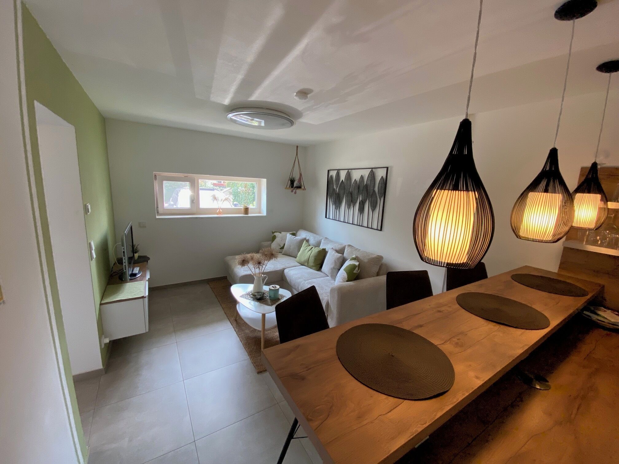 Ein modernes Wohnzimmer mit einer Couch, einem Esstisch und Pendelleuchten.