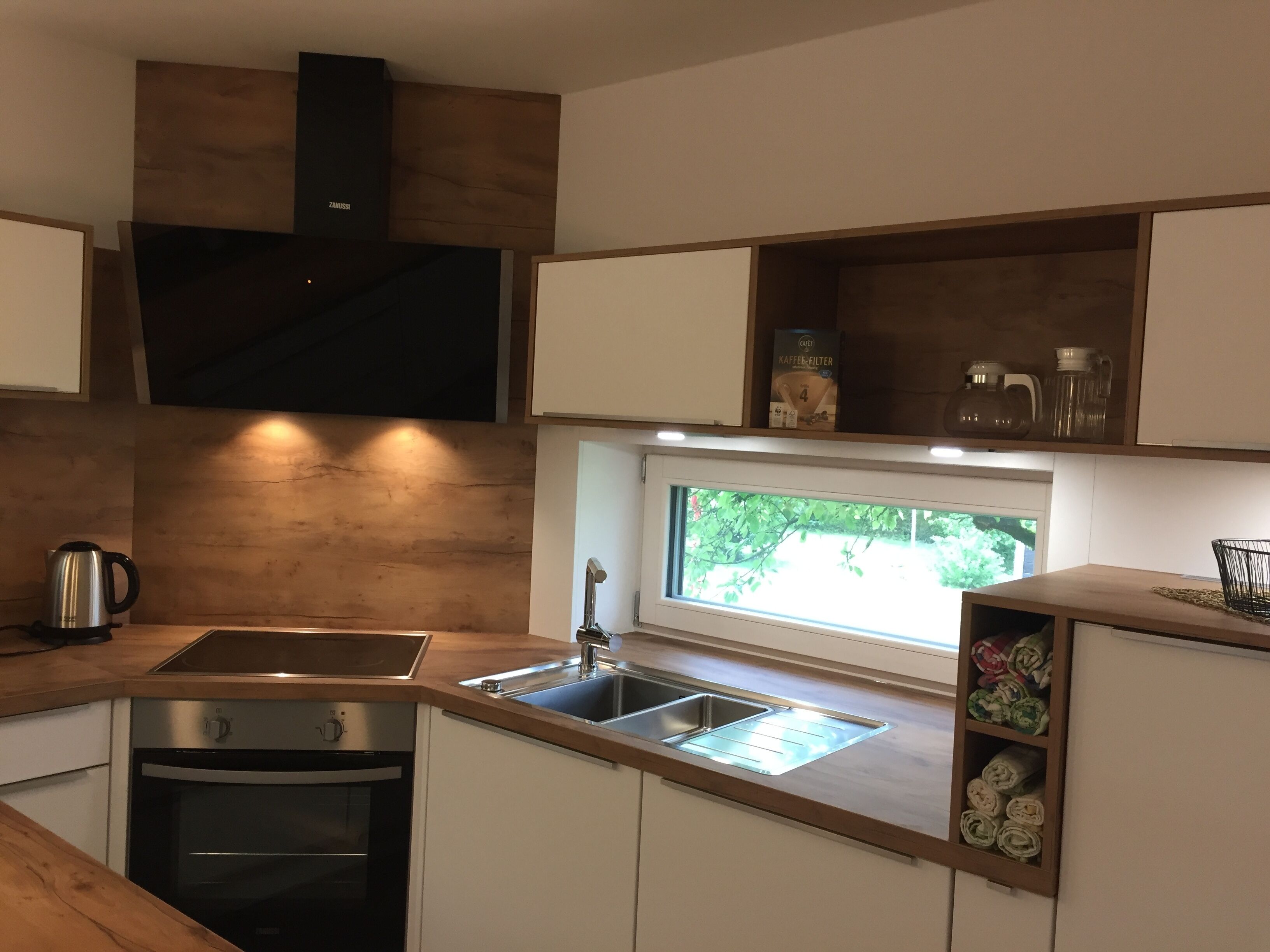 Una cocina moderna con un lavamanos de acero inoxidable, un horno empotrado y una ventana con vistas a la vegetación.