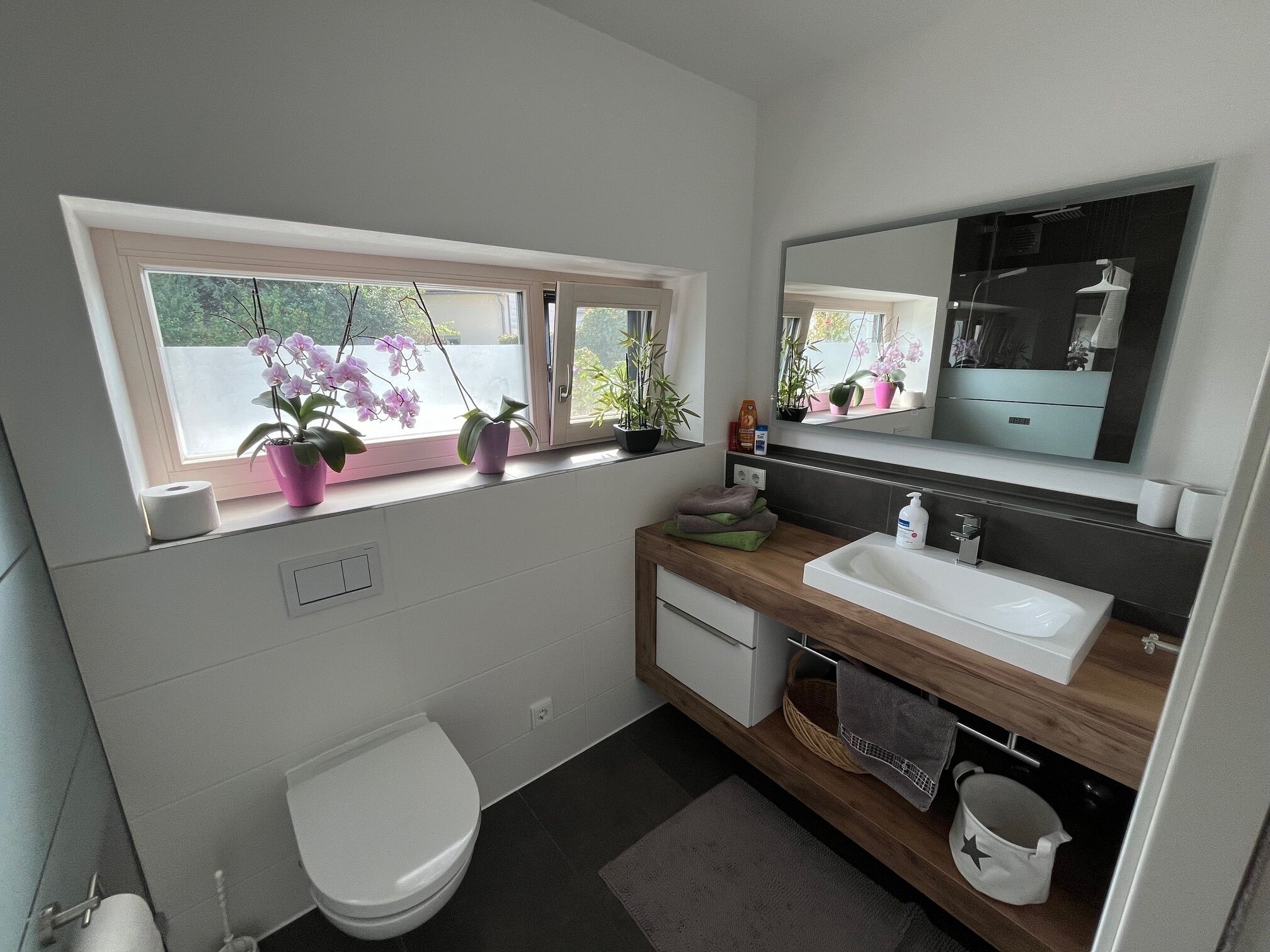 Ein modernes Badezimmer mit Toilette, Waschbecken und Fenster mit Topfpflanzen.