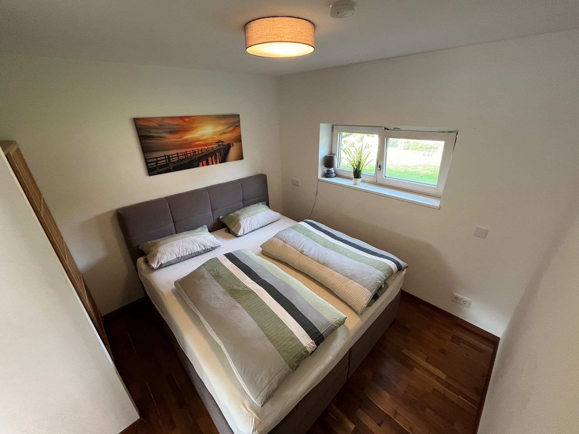 Ein Schlafzimmer mit einem Bett, einem Fenster, einem Gemälde und einer Deckenleuchte.