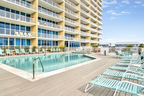 A poolside area with lounge chairs and a building with multiple balconies. - Large 3BR @ Sanibel • Sleeps 11 • Gulf Views, Poolside Location & Easy Beach Access (Gulf Shores)