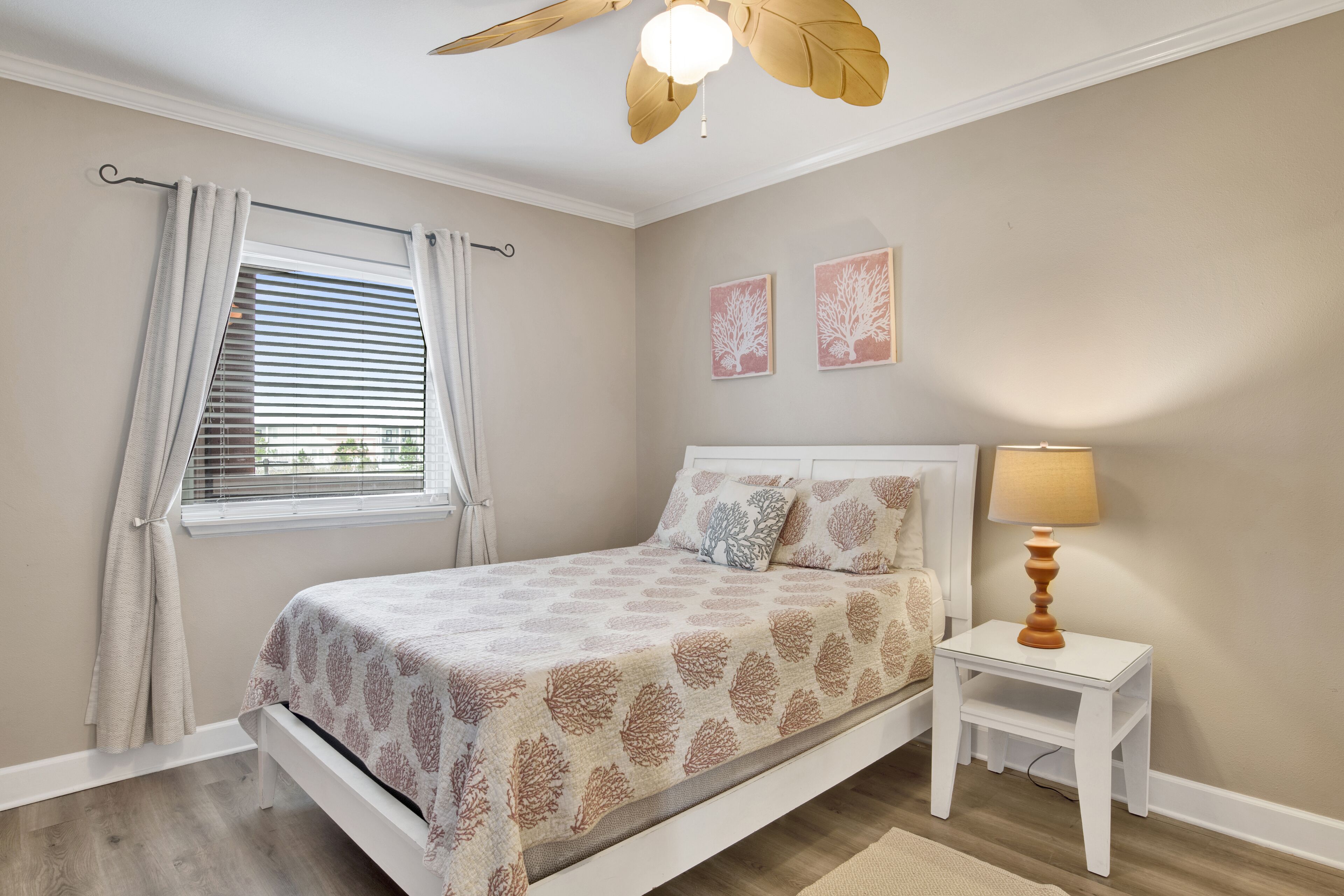 A bedroom with a bed, a nightstand with a lamp, a window with curtains, and a ceiling fan.