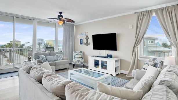 Ein modernes Wohnzimmer mit einem großen Glastisch, beigen Sofas, einer weißen Unterhaltungsecke und einem Deckenventilator.