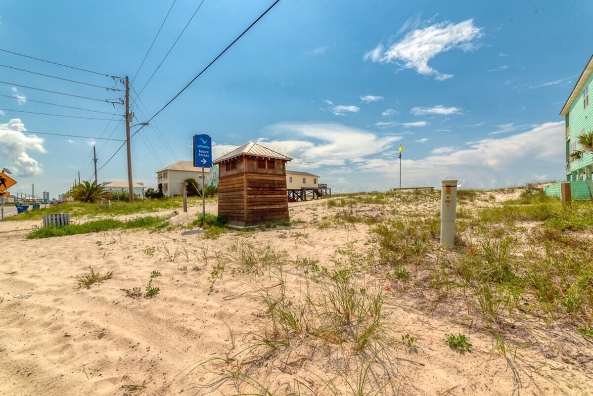 A sandy beach area with a wooden structure, a blue sign, and a building in the background.