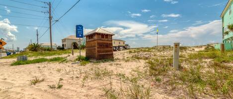 A sandy beach area with a wooden structure, a blue sign, and a building in the background.